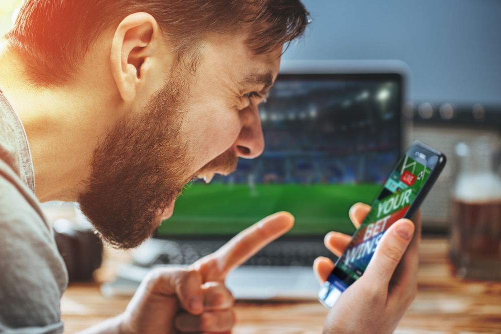 man celebrating victory after making bets using his phone